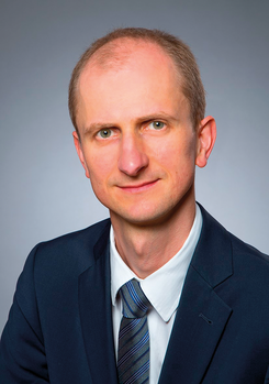 Egy személy formális öltözetben, öltönyben és nyakkendőben, homályosított arccal.