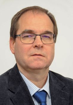 Egy férfi öltönyt és kék nyakkendőt visel, fehér csíkos inggel.