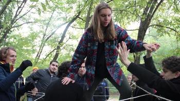 Csoport segít egy személynek átkelni egy szabadtéri kötélpályán csapatépítő tevékenység során.