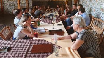 Csoport ül egy hosszú asztal körül egy étteremben, italok és jegyzetek az asztalon.
