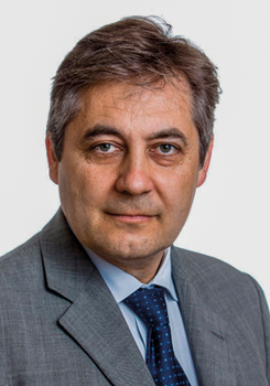 Férfi szürke öltönyben és kék nyakkendőben, a képen a felsőtest látható