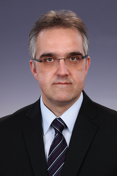Formális öltözet, sötét öltöny, fehér ing és csíkos nyakkendő látható a képen.