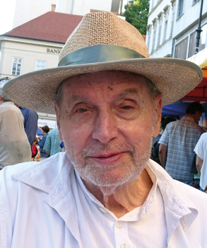 Kalapot viselő személy fehér ingben, városi környezetben emberek és épületek háttérben.