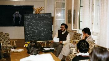 Egy férfi matematikai képleteket magyaráz egy csoportnak egy szobában.