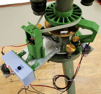 Mechanikus eszköz zöld és fém alkatrészekkel, LED-ekkel és kábelekkel egy állványon.