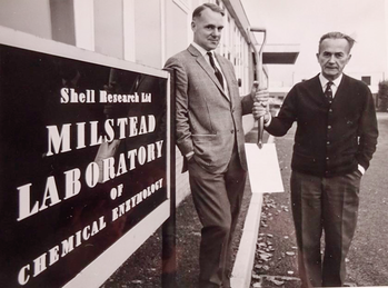 Két férfi áll a Shell Research Ltd Milstead Laboratory of Chemical Enzymology előtt, egyikük ásót tart.