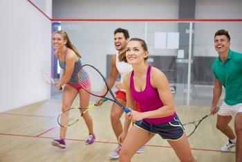 Négy ember squash-t játszik egy beltéri pályán, mindegyikük squash ütőt tart.
