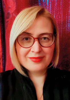 Szőke hajú nő fekete ruhában, vörös háttér előtt